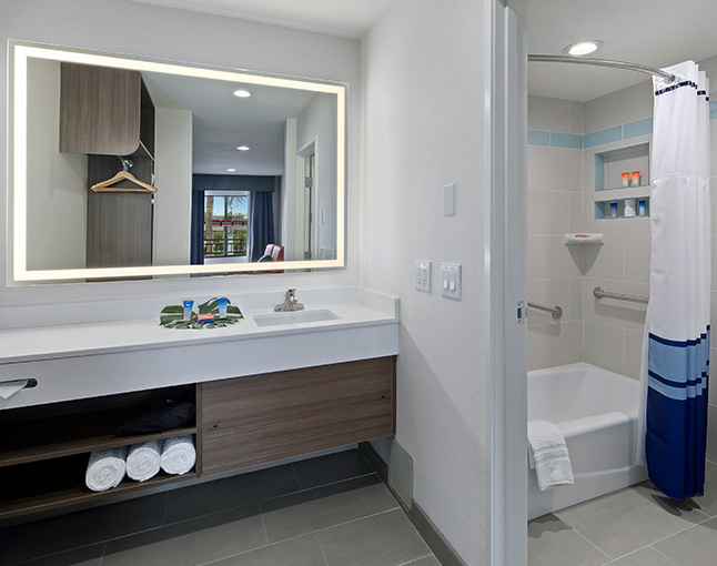 A clean bathroom with a large mirror, sink, shower, and bathtub