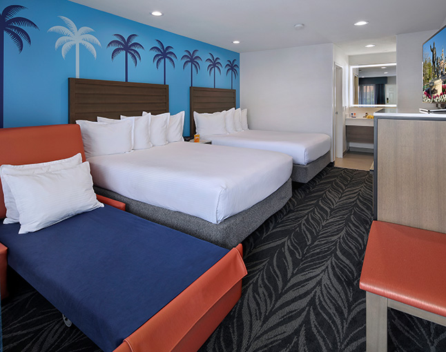A hotel room with two queen beds, a sofa bed, and a desk area.