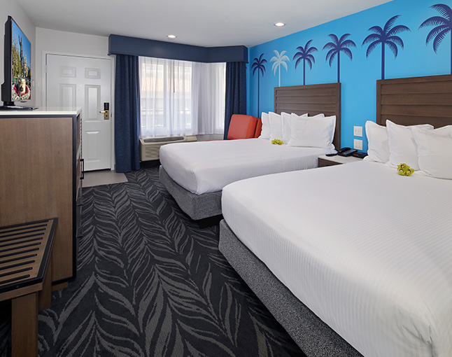 A hotel room with two queen beds, a window, a door, and a dresser with a flat-screen TV on top.