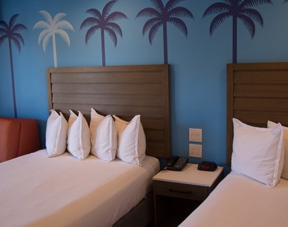 Close up of 2 queen beds and decorative palm tree wallpaper