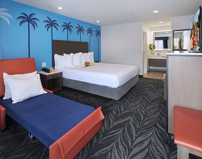 A hotel room with a king-sized bed, pullout bed, and palm tree mural on the wall.