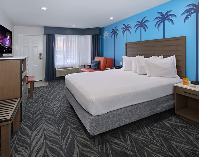 A hotel room with a king-sized bed, flat-screen TV, window, armchair, and carpeted floor.