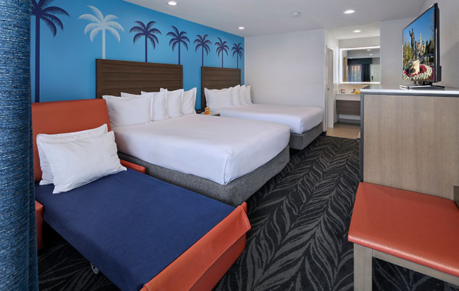A hotel room with two double beds, a sofa bed, and a kitchenette.