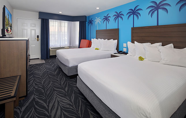 A hotel room with two double beds, a window, a dresser, and a chair.