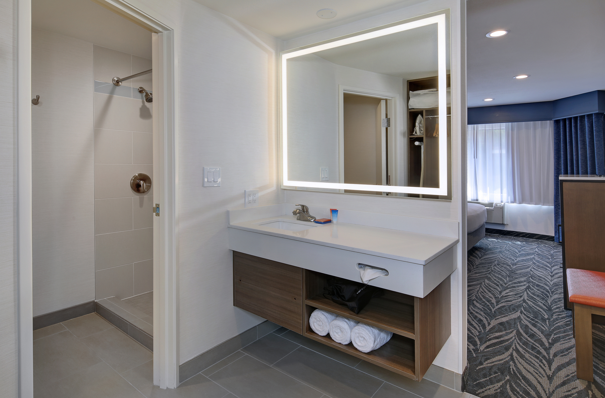 A hotel bathroom with a sink, mirror, and shower