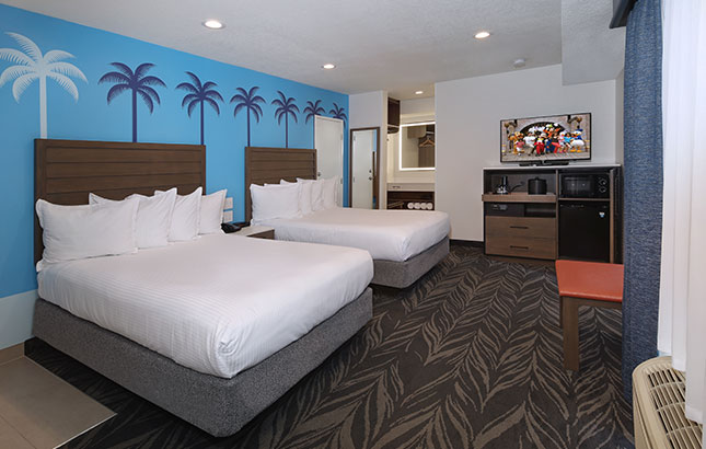 A hotel room with two beds, a TV, and a palm tree mural on the wall.