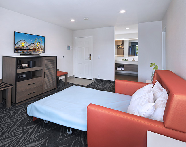 A hotel room with a pull-out sofa bed, TV, and entertainment center.