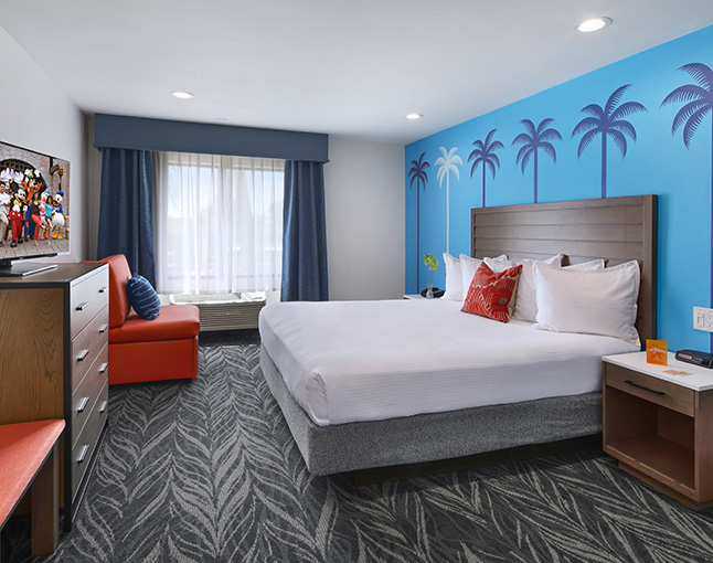 A hotel room with a large bed, orange chair, and window