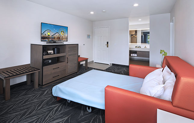 A hotel room with a sofa bed, TV, and wooden furniture.