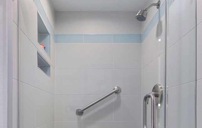 A bathroom shower with gray tile, a grab bar, and a glass door.