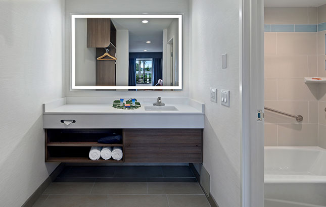 A bathroom vanity with a large mirror, sink, and towels, with a bathtub visible in the background.