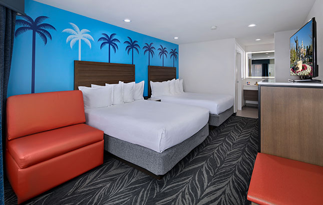 A hotel room with two double beds, a red sofa, and a TV on a wooden cabinet.