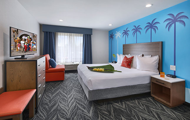 A wide view of a hotel room with a king-sized bed, dresser, armchair, and TV.