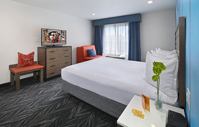 A hotel room with a bed, TV, dresser, chair, and window