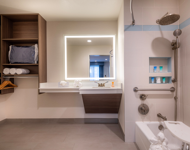 A clean and modern bathroom with a large mirror, shower, bathtub, and shelves.