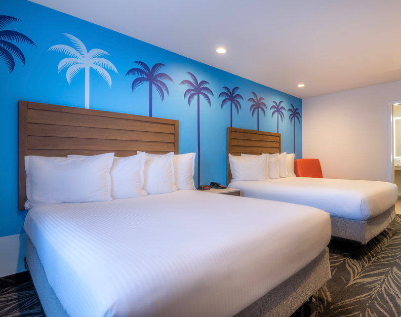 A hotel room with two queen beds, wood headboards, and a blue wall with palm tree designs.