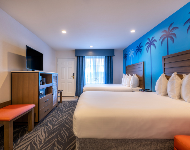A hotel room with two double beds, a flat screen TV on a dresser, and a window with blue curtains.