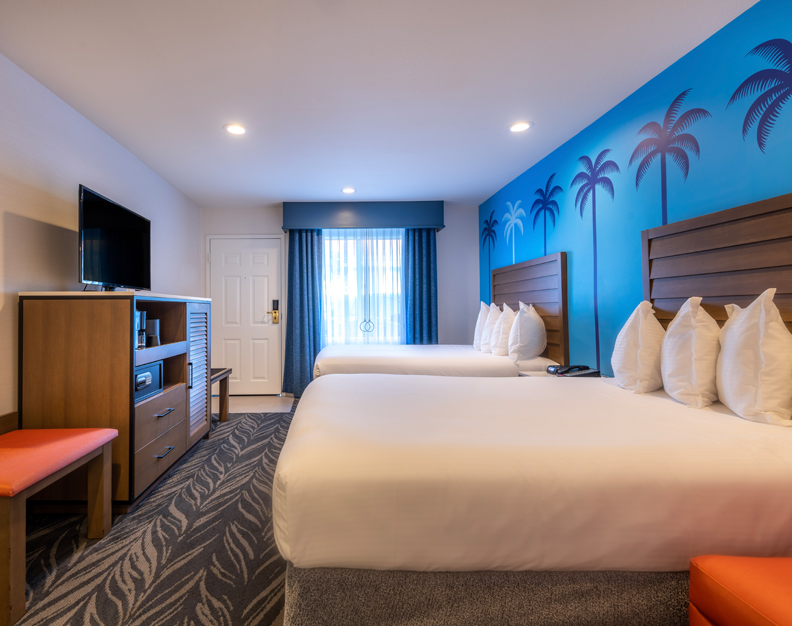 A hotel room with two double beds, a TV on a dresser, and a window with blue curtains.