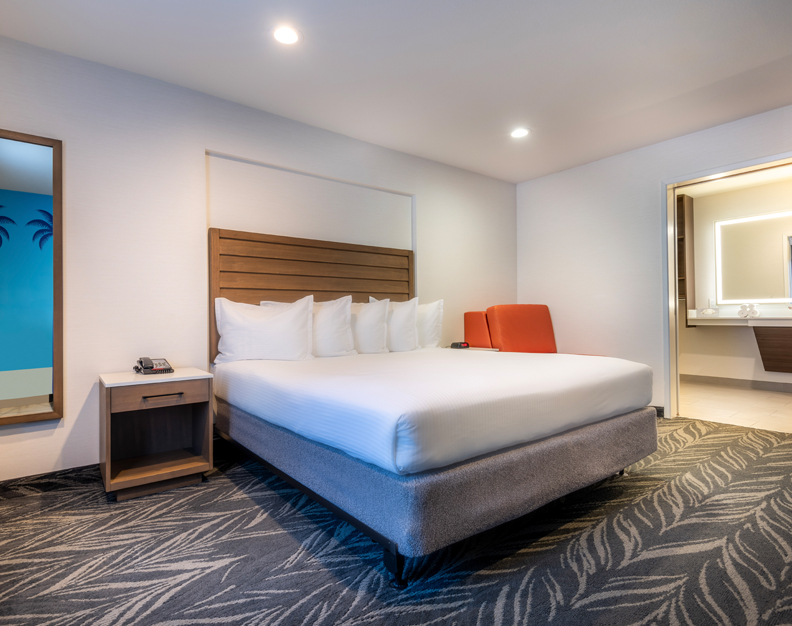 A hotel room with a king-sized bed, nightstand, chair, and partial view of the bathroom.