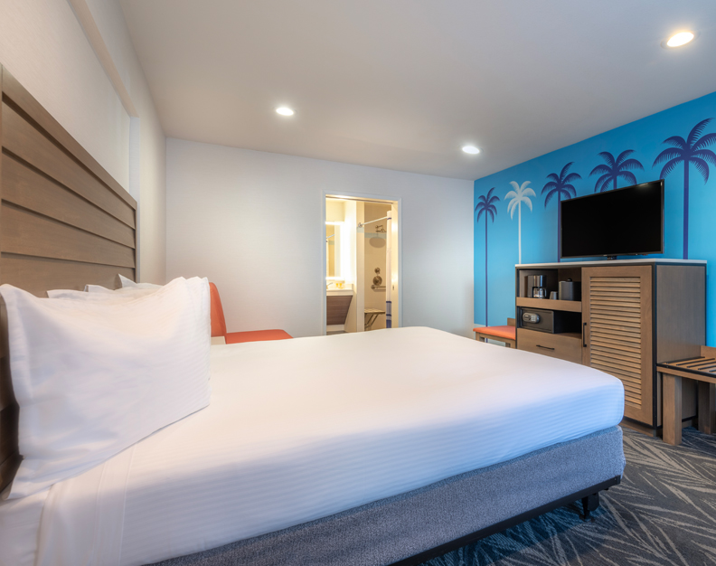 A hotel room with a king-sized bed, wooden headboard, and palm tree mural on one wall.