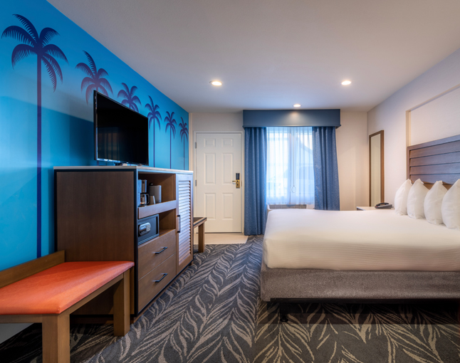 A hotel room with a large bed, wooden furniture, and palm tree wallpaper.
