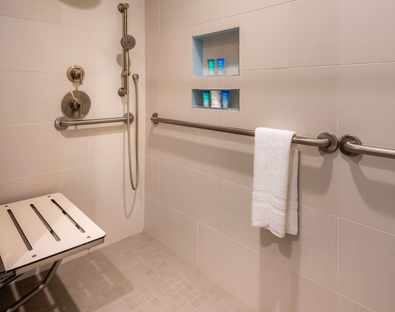 A tiled roll-in shower with grab bars, a seat, and toiletries.