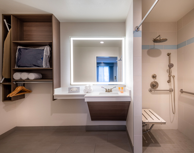 A modern bathroom with a large mirror, sink, and walk-in shower with a bench.
