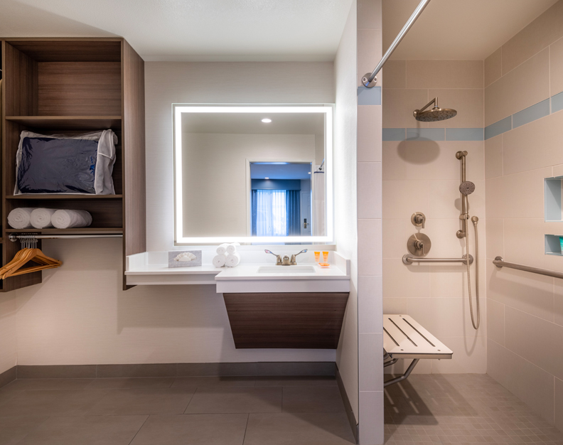 A modern bathroom with a large mirror, a shower with a bench, and a sink.